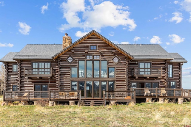 rear view of house featuring log exterior, a chimney, and a wooden deck