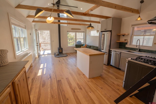 kitchen featuring a sink, wood counters, vaulted ceiling with beams, a wood stove, and stainless steel appliances