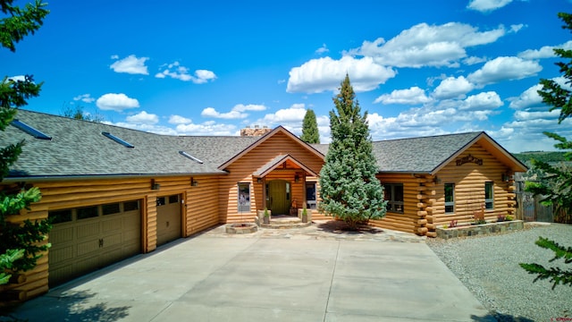 cabin featuring driveway, roof with shingles, log exterior, and a garage