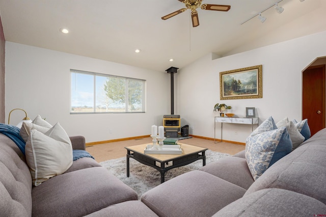 living room featuring vaulted ceiling, baseboards, light colored carpet, a ceiling fan, and a wood stove
