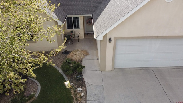 exterior space featuring a garage, concrete driveway, roof with shingles, and stucco siding