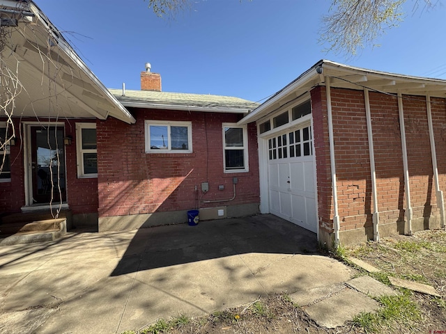 212 Bell Ave, Alamosa, CO 81101 - view of home's exterior with a chimney, brick siding, a garage, and concrete driveway