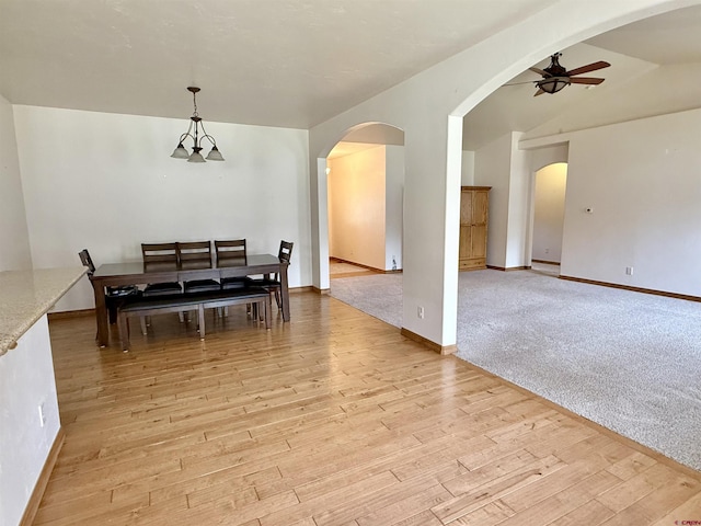 dining space featuring arched walkways, light wood-style flooring, vaulted ceiling, ceiling fan, and baseboards