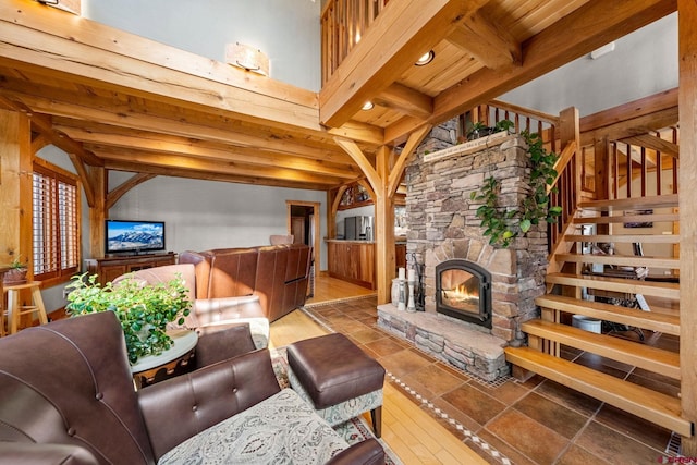 living room featuring a stone fireplace, wood finished floors, beamed ceiling, and stairs