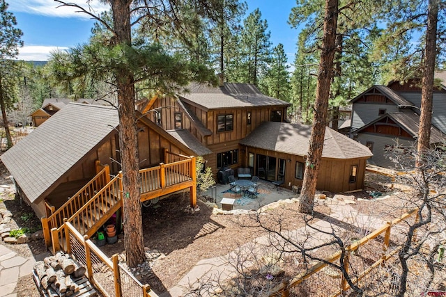 rear view of house with board and batten siding, a patio, a wooden deck, roof with shingles, and stairs