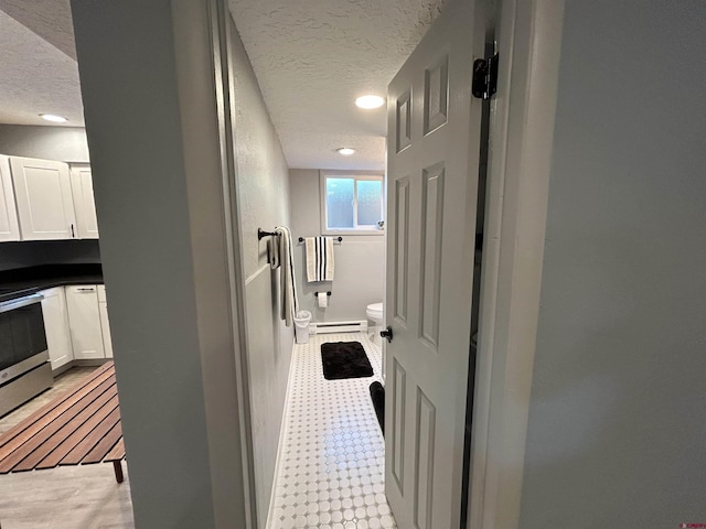 hallway featuring light floors, a baseboard heating unit, a textured ceiling, and recessed lighting