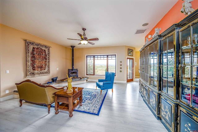 living room featuring baseboards, a ceiling fan, a wood stove, and light wood-type flooring