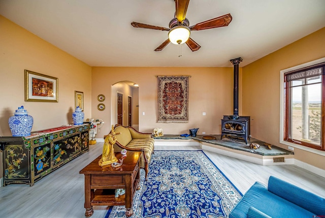living area with arched walkways, ceiling fan, wood finished floors, and a wood stove