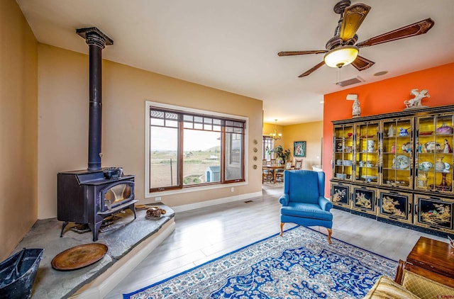 living area featuring visible vents, wood finished floors, a wood stove, and ceiling fan with notable chandelier