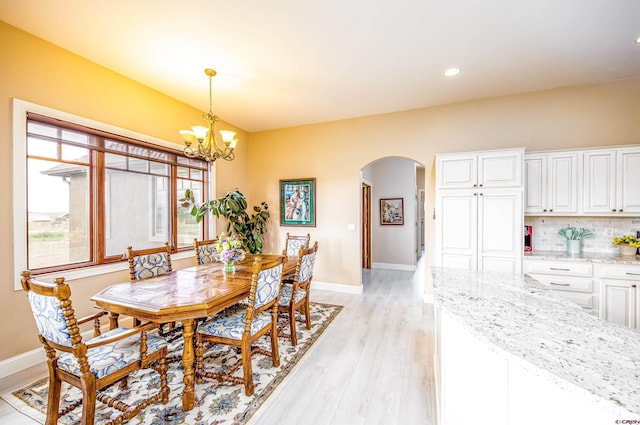 dining space featuring light wood-style floors, arched walkways, baseboards, and a chandelier