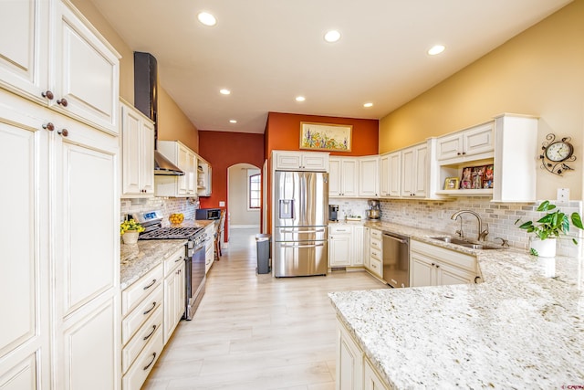 kitchen featuring appliances with stainless steel finishes, light stone counters, a sink, arched walkways, and backsplash