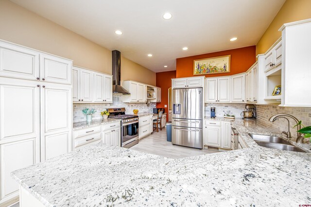 kitchen featuring wall chimney range hood, appliances with stainless steel finishes, open shelves, light stone countertops, and a sink