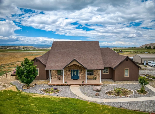 view of front of property with a shingled roof, covered porch, and stone siding