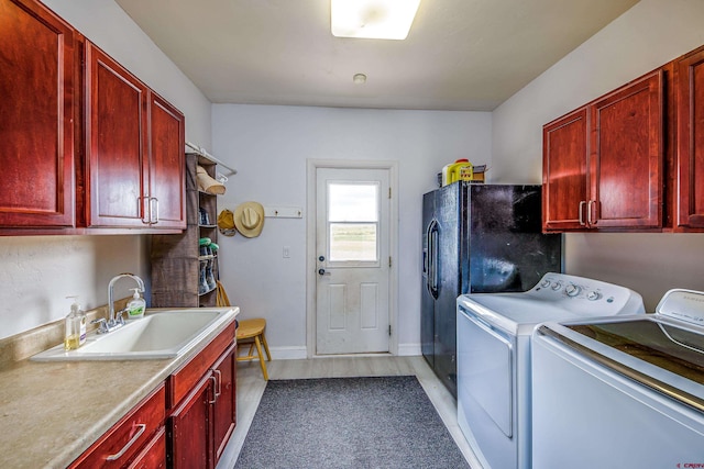 clothes washing area featuring a sink, baseboards, cabinet space, and washer and clothes dryer
