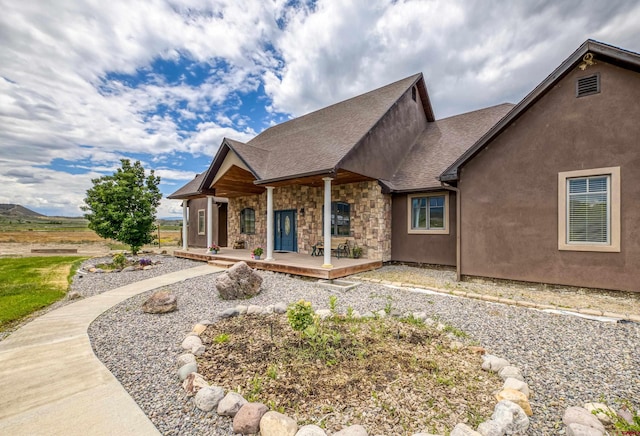 view of front of house featuring covered porch, roof with shingles, and stone siding