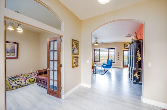 corridor with arched walkways, baseboards, wood finished floors, and visible vents
