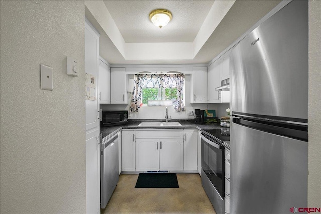 kitchen with white cabinets, a textured wall, appliances with stainless steel finishes, dark countertops, and a sink