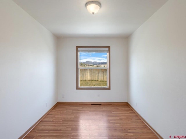 spare room with baseboards, visible vents, and wood finished floors