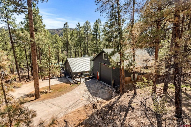 exterior space with a view of trees, metal roof, and dirt driveway