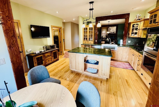 kitchen with a kitchen island, dark countertops, glass insert cabinets, tasteful backsplash, and light wood finished floors