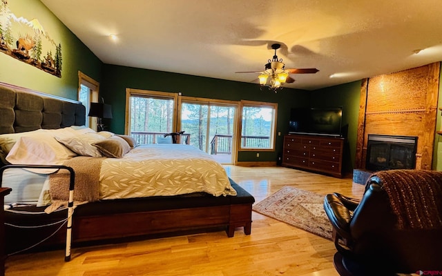 bedroom featuring access to outside, a ceiling fan, wood finished floors, and a fireplace