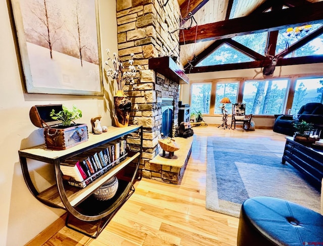 living area with a high ceiling, beam ceiling, a stone fireplace, baseboards, and wood finished floors