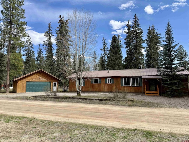 single story home with a garage, dirt driveway, an outbuilding, and metal roof