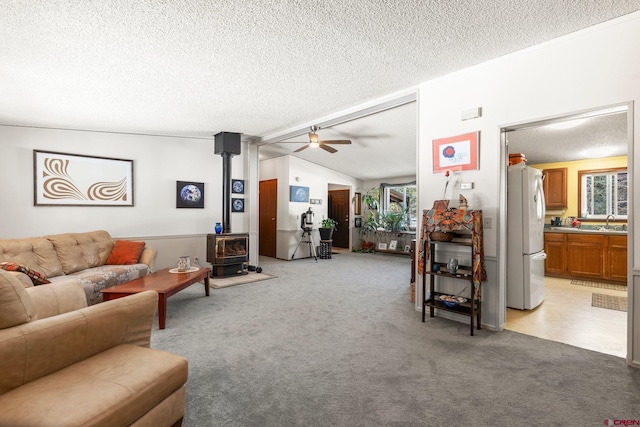 living room featuring a ceiling fan, a textured ceiling, light colored carpet, and a wood stove