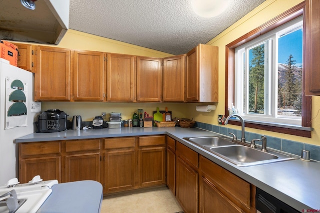 kitchen with a sink, vaulted ceiling, brown cabinets, and a textured ceiling