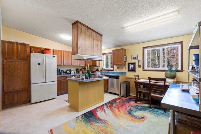 kitchen featuring brown cabinetry, freestanding refrigerator, a center island, a textured ceiling, and dishwasher