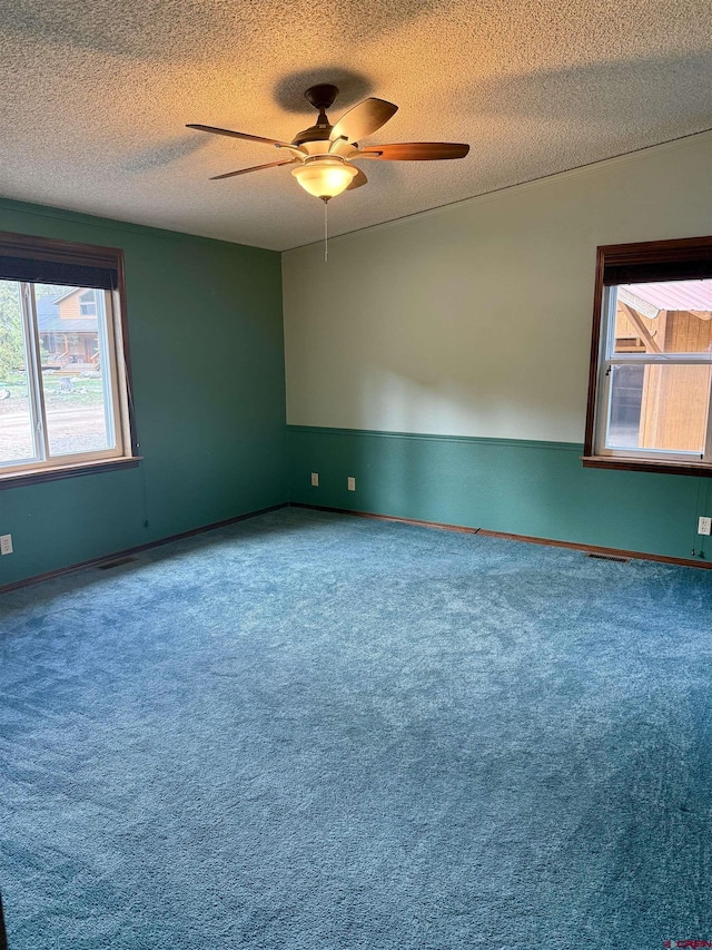 carpeted empty room featuring baseboards, ceiling fan, a textured ceiling, and a wealth of natural light