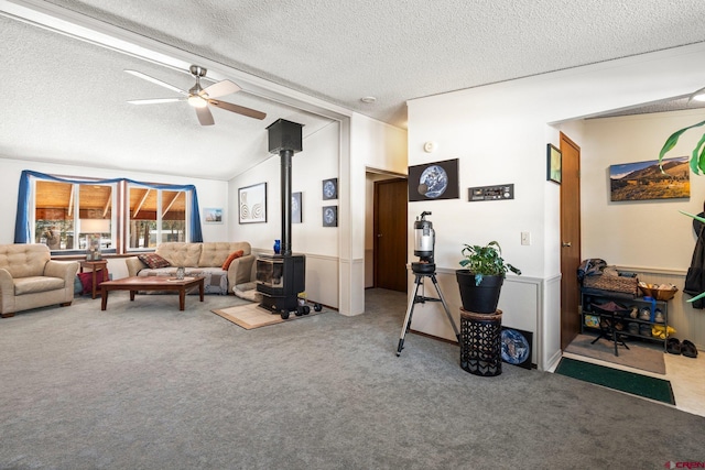 living room featuring ceiling fan, a textured ceiling, a wood stove, lofted ceiling, and carpet