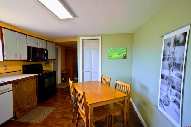 kitchen featuring dark wood-style flooring, dishwasher, light countertops, baseboards, and black range with electric stovetop