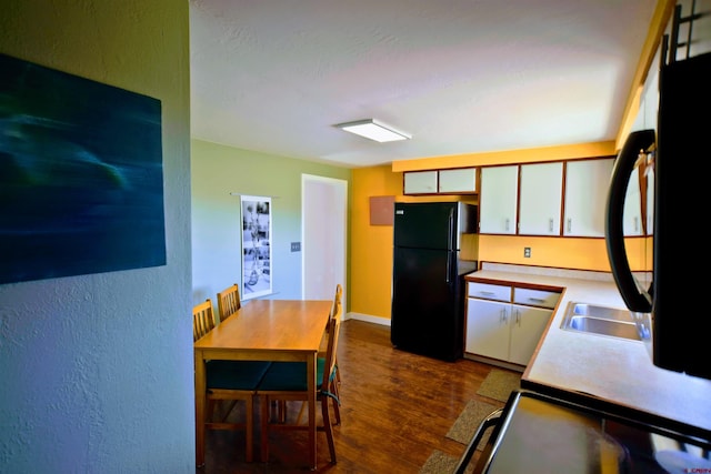 kitchen featuring fridge, a textured wall, light countertops, freestanding refrigerator, and dark wood-style floors