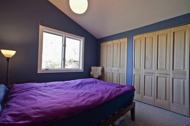 bedroom with carpet, vaulted ceiling, and two closets