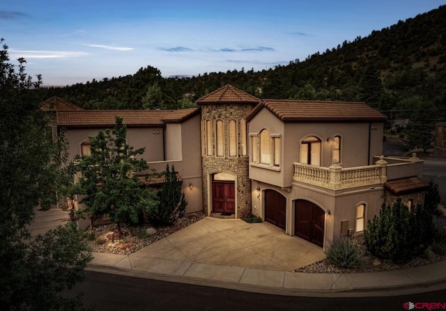 mediterranean / spanish-style home featuring an attached garage, stucco siding, driveway, and stone siding