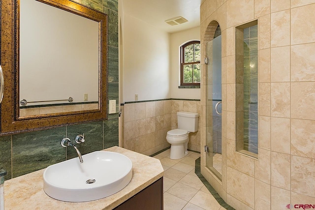 bathroom with tile walls, a stall shower, vanity, tile patterned floors, and toilet