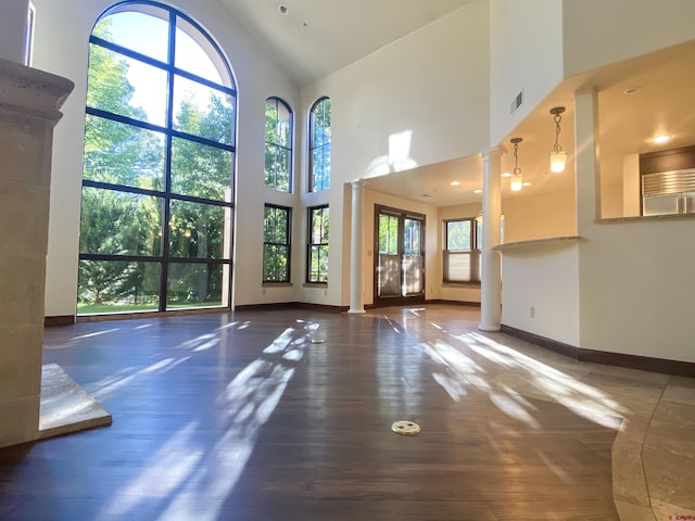 unfurnished living room with visible vents, wood-type flooring, decorative columns, baseboards, and high vaulted ceiling