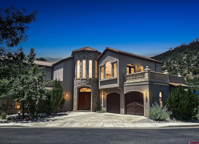 mediterranean / spanish house featuring a tiled roof, a balcony, concrete driveway, an attached garage, and stucco siding