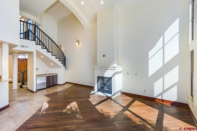 unfurnished living room with visible vents, arched walkways, high vaulted ceiling, baseboards, and a glass covered fireplace