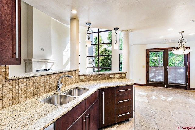 kitchen featuring baseboards, a sink, decorative backsplash, and light stone countertops