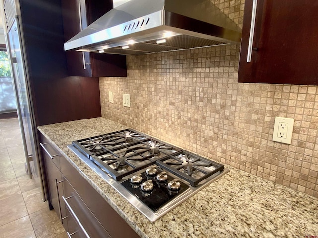 kitchen featuring backsplash, range hood, stainless steel gas cooktop, light stone countertops, and light tile patterned floors