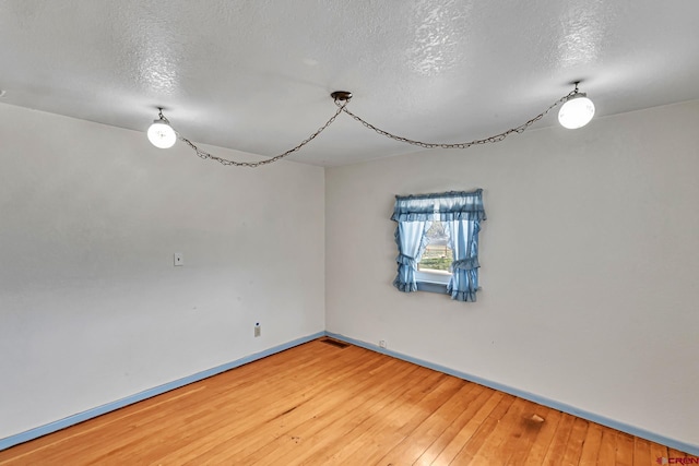 unfurnished room with a textured ceiling, baseboards, and hardwood / wood-style flooring
