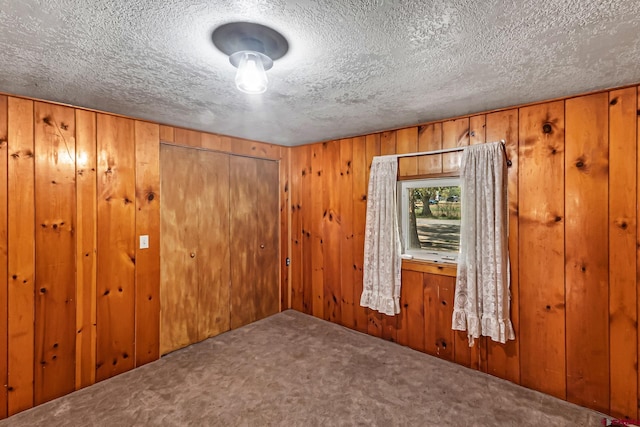 carpeted spare room featuring wooden walls and a textured ceiling