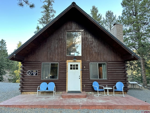 rear view of house with log exterior, a chimney, and a patio area