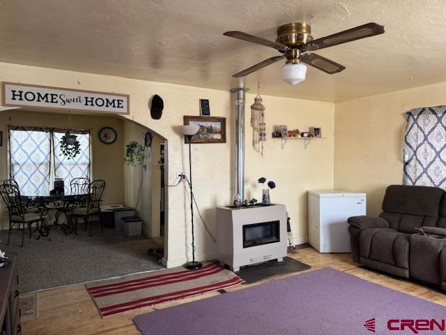 living area featuring arched walkways, a textured ceiling, ceiling fan, and wood finished floors