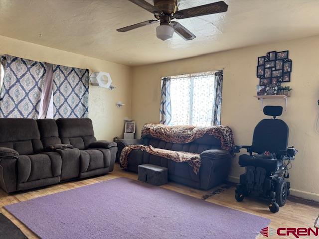 living room featuring a ceiling fan, baseboards, and wood finished floors