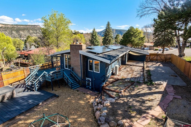 view of side of property featuring an attached carport, a deck with mountain view, a fenced backyard, a chimney, and solar panels