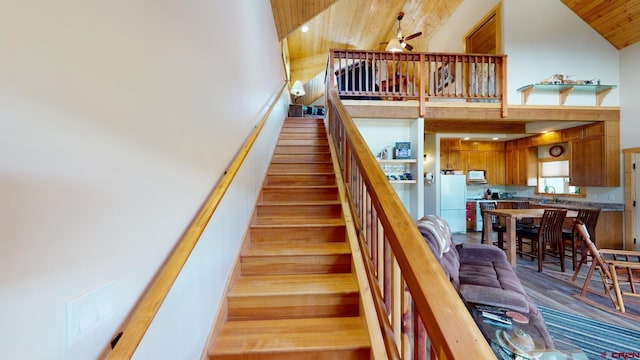 stairs with a ceiling fan, high vaulted ceiling, wood ceiling, and wood finished floors