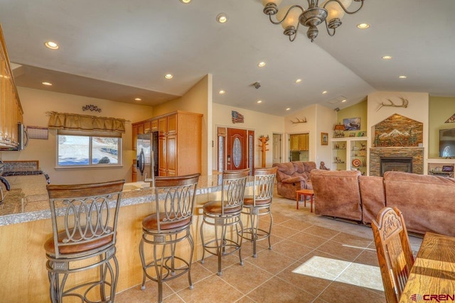 kitchen with a kitchen breakfast bar, vaulted ceiling, light tile patterned floors, stainless steel fridge, and recessed lighting